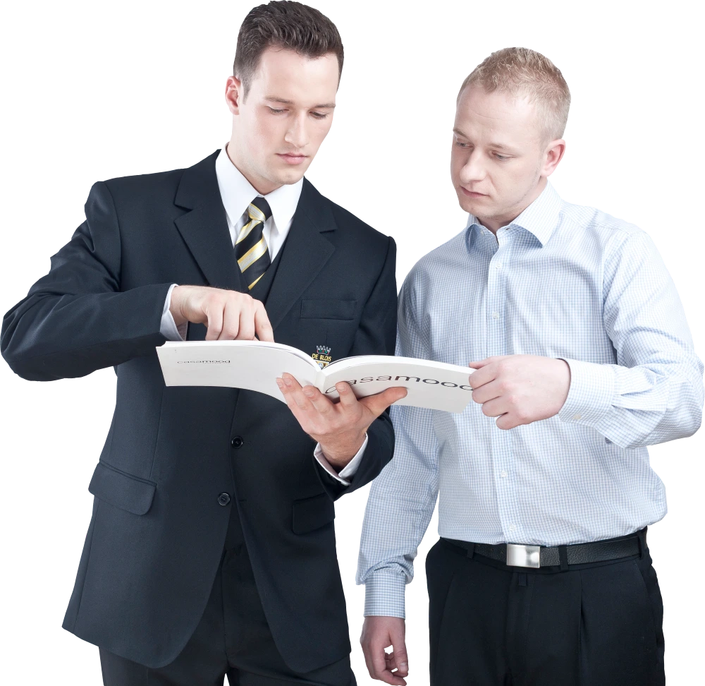 Zwei Männer in Anzug und Hemd betrachten zusammen ein aufgeschlagenes Buch oder Magazin.