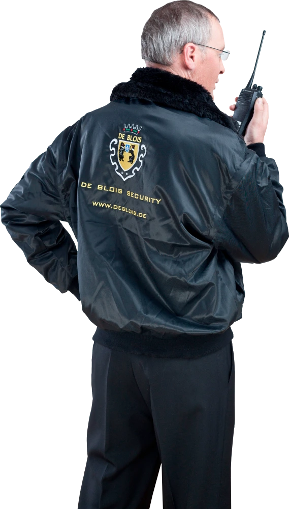Mann in schwarzer Jacke mit De Blois Security-Logo, hält Funkgerät am Ohr.